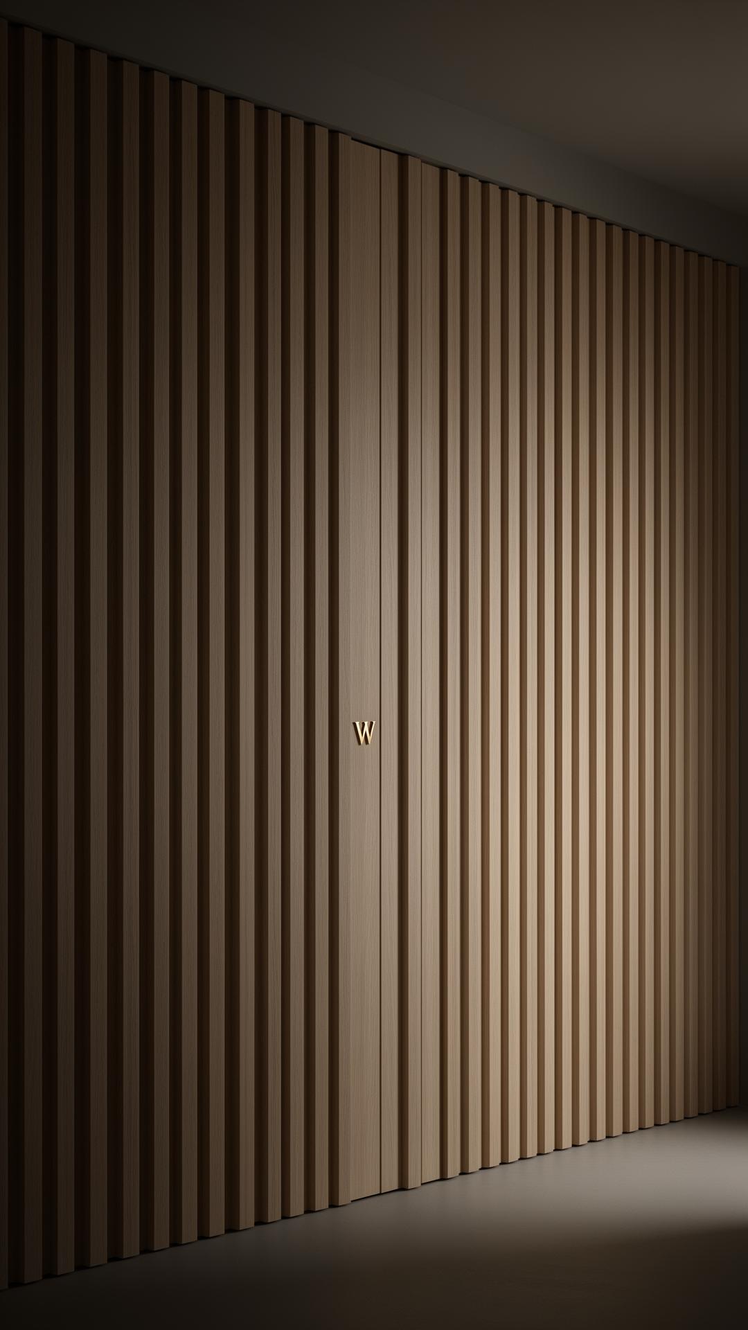 A pale oak slat wall with a barely visible vertical seam concealing a pivot door, marked only by a small brushed-brass W